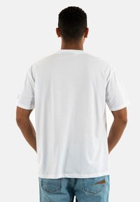 Camiseta blanca de algodón con mangas cortas, cuello redondo y un corte relajado. La vista trasera no muestra patrones, tiene una textura suave y un mínimo de detalles.