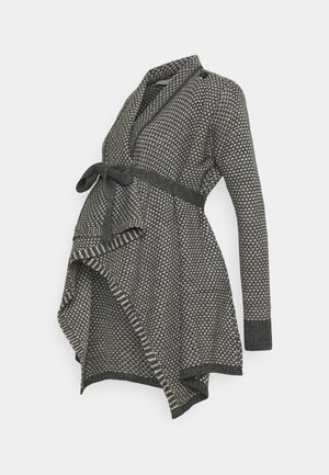 Tummanharmaa neulottu äitiysneuletakki, jossa valkoinen pilkullinen kuvio, pitkät hihat, huivikaulus ja solmittava vyö.