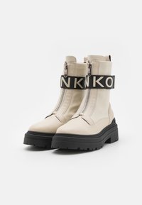 Crème-kleurige enkellaarsjes van glad leer met een robuuste zwarte rubberen zool en een contrasterende elastsband met gedurfde lettering.
