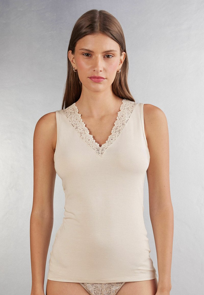Top sin mangas color beige con cuello en V y detalle de encaje en el escote. Fabricado con un tejido suave para una silueta ajustada.