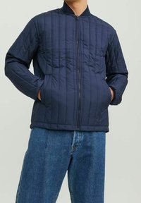 Marinblå vadderad jacka gjord av syntetiskt material, med dragkedja fram, ribbad krage och två sidofickor. Avslappnad passform.