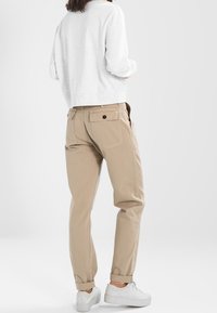 Chinos beige, ajustados con bolsillos traseros y cierre de botón, combinados con una sudadera gris claro y zapatillas blancas. Textura suave.