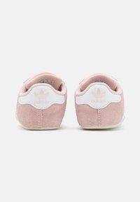 Zapatillas adidas de ante rosa con suelas de goma blanca. Entre sus características se incluyen un parche con el logo blanco en el talón y un forro de tejido texturizado.