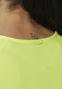 Helder neon geel, geribbelde stof met een ronde halslijn en een naaddetail. Een kleine tattoo is zichtbaar op de nek.