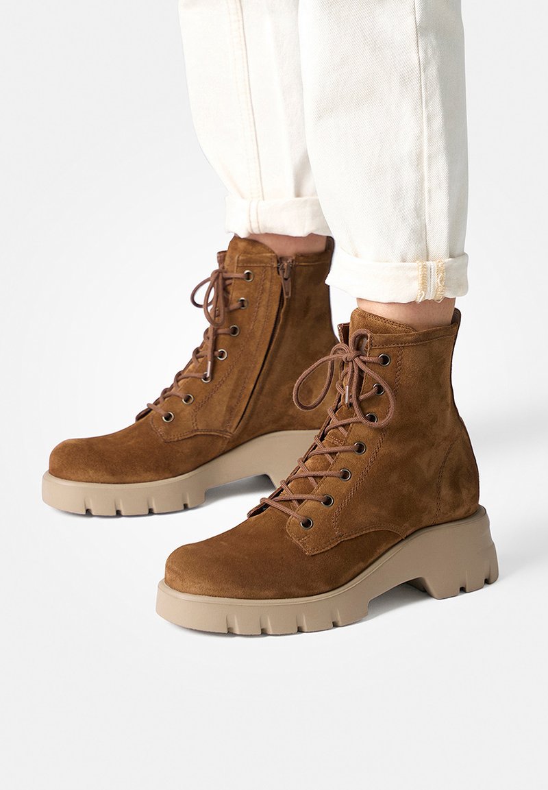 Brown suede lace-up ankle boots with side zipper and chunky beige soles worn with rolled-up white pants.