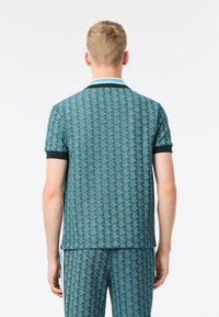 Grönmönstrad piké med en texturerad design, kontrasterande mörkgrön krage, korta ärmar och en avslappnad passform.