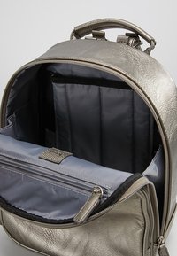 Metaliczny srebrny plecak z główną komorą zamykaną na zamek błyskawiczny, wyściełanymi przegródkami i szarą podszewką wewnętrzną. Posiada górny uchwyt i boczne akcenty.