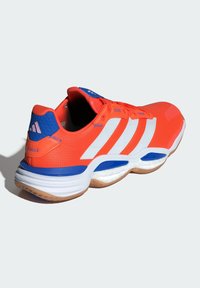 Oranžová sportovní bota s bílými pruhy, modrými akcenty a texturovaným síťovaným svrškem. Obsahuje polstrovanou podrážku a design zaoblené paty.