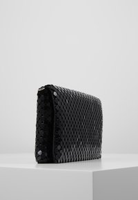 Musta kuusikulmainen clutch, joka on valmistettu kiiltävästä materiaalista, ja siinä on tyylikäs suorakulmainen muoto ja sileä pintakuvio. Näytetään sivulta.