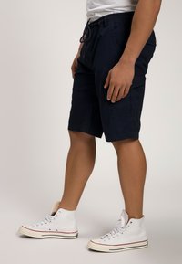 Shorts cargo navy avec une taille élastique, cordon de serrage, poches latérales et une coupe droite. Associés à des baskets blanches montantes.