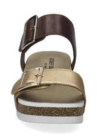 Gold- und braune Leder-Sandale mit einem breiten Riemen, großer silberner Schnalle, gepolstertem Fußbett und einer strukturierten Kork-Zwischensohle. Weißer Sohlenrand.