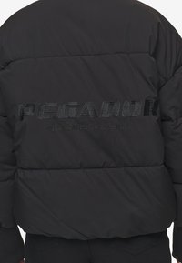 Giacca a vento nera con la scritta "PEGADOR" e "CERTIFIED AUTHENTIC STREETWEAR" in rilievo sul retro. Tessuto testurizzato e design isolato.