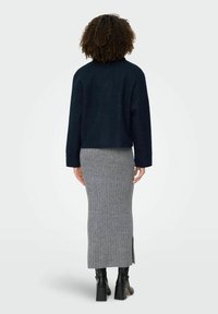 Mornarska teksturirana skraćena jakna preko sive rebraste pletene midi suknje s bočnim prorezima, uparenih s crnim čizmama do gležnja na blok petu.