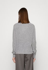 Maglione grigio a coste con maniche lunghe, scollo rotondo e vestibilità comoda. Il tessuto appare morbido con dettagli testurizzati lungo le cuciture.