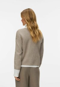 Beežist kootud kampsun valgete soonikkoes ääre ja mansettidega. Omadusena on sellel lõõgastunud lõige ja tekstuuriga muster, kantud kõrge vöökohaga pükste peale.