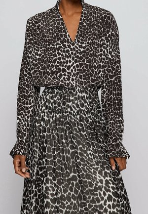 Schwarz-weißes Leopardenmuster Kleid mit langen Ärmeln, geraffter Taille und V-Ausschnitt, getragen von einer Person vor neutralem Hintergrund.