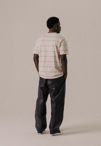 T-shirt a maniche corte a righe di colore beige chiaro con strisce arancioni, abbinato a pantaloni in pelle nera dal taglio morbido. Design semplice e vestibilità comoda.