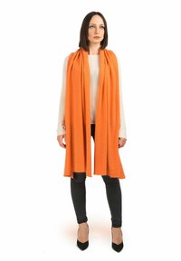 Orange tørklæde lavet af blødt stof, der hænger elegant, parret med en lys top og sorte jeans, båret med spidse sorte hæle.
