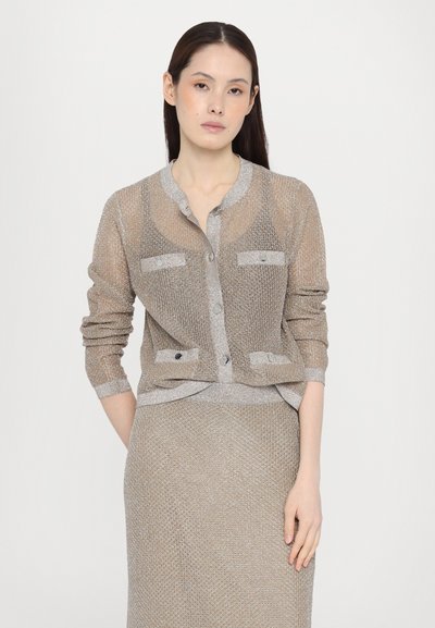Beige neulecardigan hopeakiilloilla, jossa on pyöreä kaula-aukko, nappisulku ja kaksi etutaskua. Kankaan tekstuuri on hienovarainen hohde.