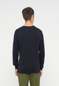 Sweater de malha azul-marinho com mangas longas, decote redondo, punhos e bainha canelados. Textura suave e ajuste casual. Usado sobre calças verde-azeitona.