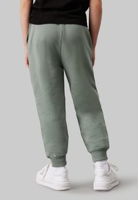 Pantaloni sportivi verdi realizzati in morbido tessuto, con un design affusolato e polsini a coste. Abbinati a sneakers bianche e una maglietta nera.