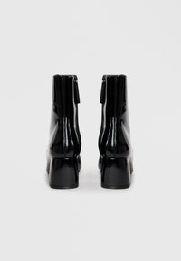 Schwarze Lackleder-Stiefeletten mit quadratischer Zehenform, erhöhtem Absatz und Reißverschluss auf der Rückseite. Glatte, glänzende Oberfläche.
