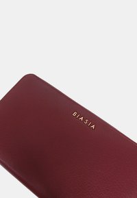 Portafoglio in pelle bordeaux con superficie texturizzata e logo "BIASIA" in oro stampato. Forma rettangolare con angoli arrotondati.
