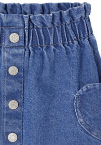 Blauer Denim-Stoff mit gerafftem Elastikbund, Metall-Druckknöpfen vorne und einer abgerundeten Fronttasche mit orangefarbener Naht.