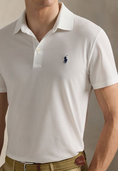 Λευκή μπλούζα πόλο με υφασμάτινη υφή, διαθέτει γιακά με κολάρο, πατιλέτα με δύο κουμπιά και ναυτικό λογότυπο στο αριστερό στήθος.