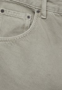 Tessuto di denim grigio chiaro che mostra un primo piano di una tasca anteriore con rivetti metallici, dettagli di cucitura e una texture liscia.