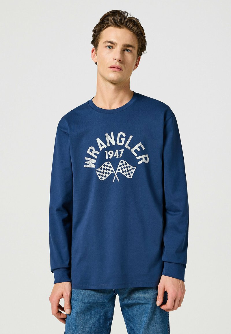 Granatowa koszulka z długim rękawem wykonana z bawełny. Posiada grafikę z przodu z napisem "WRANGLER" i flagami szachownicowymi. Okrągły dekolt i luźny krój.