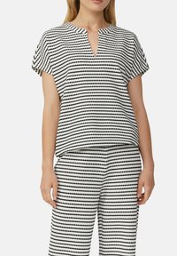 Bluzka z krótkim rękawem w czarno-białym materiale z geometrycznym wzorem. Posiada dekolt w serek i luźny krój, zestawiona z pasującymi spodniami.