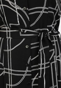 Black dress with a white geometric line pattern, featuring a tied waist, buttons down the front, and textured fabric.