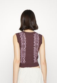Brown sleeveless sweater with purple geometric patterns on the back, featuring ribbed hem and shoulder seams. Knitted texture.