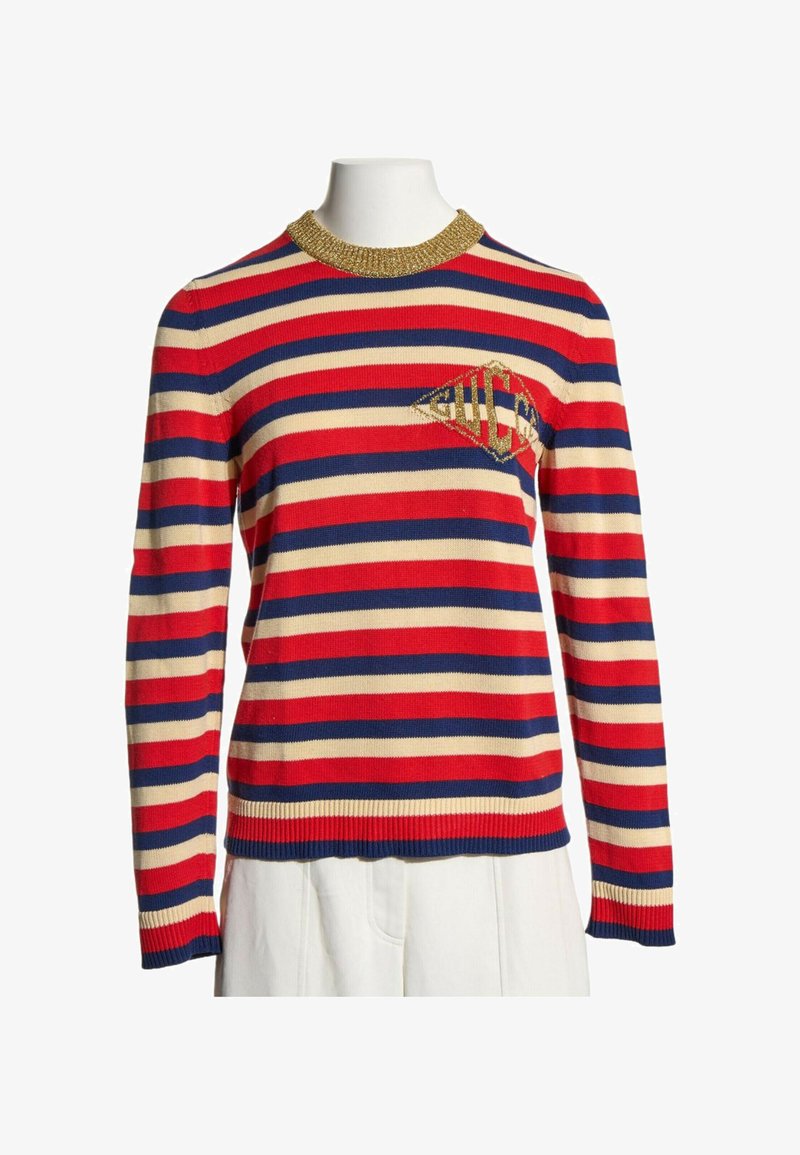 Pull à manches longues avec des rayures horizontales rouges, bleu marine et crème, col côtelé doré et logo doré en forme de diamant sur la poitrine.