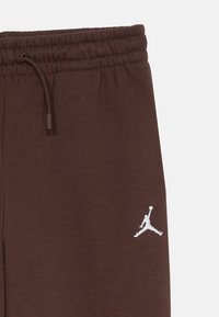 Hnedé tepláky s elastickým pásom, na nohavici s bielym vyšívaným logom Jumpman a detailom na šnúrku.