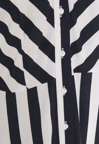 Camicia a righe con strisce verticali blu navy e bianche, caratterizzata da una chiusura frontale con bottoni e un tessuto morbido.