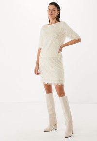 Biała sztuczna futrzana bluzka z krótkimi rękawami w komplecie z dopasowaną ołówkową spódnicą. Całość dopełniają beżowe skórzane botki na słupku sięgające do kolan.