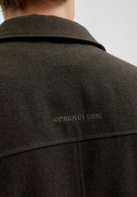 Tamnosmeđa jakna od vune s dodatkom, s definiranim ovratnikom, vidljivim šavovima i suptilnim logom "© PROJECT CORE" blizu izreza.