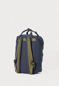 Marinblå canvasryggsäck med gröna detaljer, justerbara remmar, handtag på toppen och sidoficka för förvaring. Enkel och funktionell design.