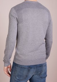 Grauer Strickpullover mit gerippten Schulterakzenten, langen Ärmeln und Rundhalsausschnitt, kombiniert mit blauen Jeans. Die Textur ist glatt.