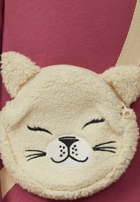 Runde, beige Beutel-Tasche mit einem strukturierten, flauschigen Äußeren, das einem Katzenkopf nachempfunden ist. Sie verfügt über gestickte Gesichtszüge und einen Reißverschluss.