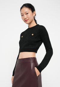 Μαύρο κοντό πουλόβερ με υφή, διαθέτει δύο μπροστινές τσέπες και χρυσά κουμπιά. Φοριέται με μια μπορντό δερμάτινη φούστα.