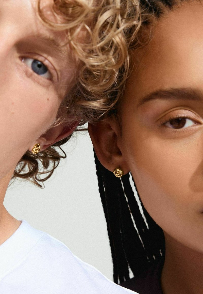 Goldene Steckerohrringe mit einem strukturierten, minimalistischen Design, kombiniert mit Personen mit lockigen und geflochtenen Frisuren vor einem neutralen Hintergrund.