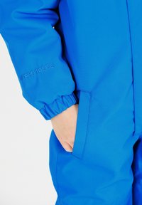 Heldere blauwe waterdichte overall met elastische manchetten, voorzien van een zijzak en een reliëfdetail "HYDRO10000" op de mouw. Soepele textuur.