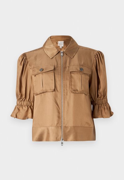 Kurze Jacke aus hellbraunem Satin. Mit einem Reißverschluss, zwei Brusttaschen und Raffung an den Ärmeln für zusätzliche Struktur.