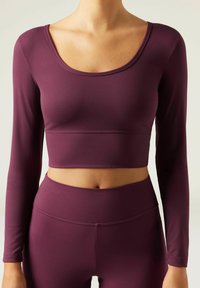 Bordeauxfarbener langärmeliger Crop-Top aus elastischem Material, mit rundem Halsausschnitt und taillierter Passform, kombiniert mit hochtaillierten Leggings.