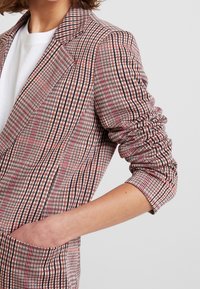 Blazer med ett rutmönster i rött, svart och vitt, med en enda ficka, skräddarsydd passform och textil i ärmarna.