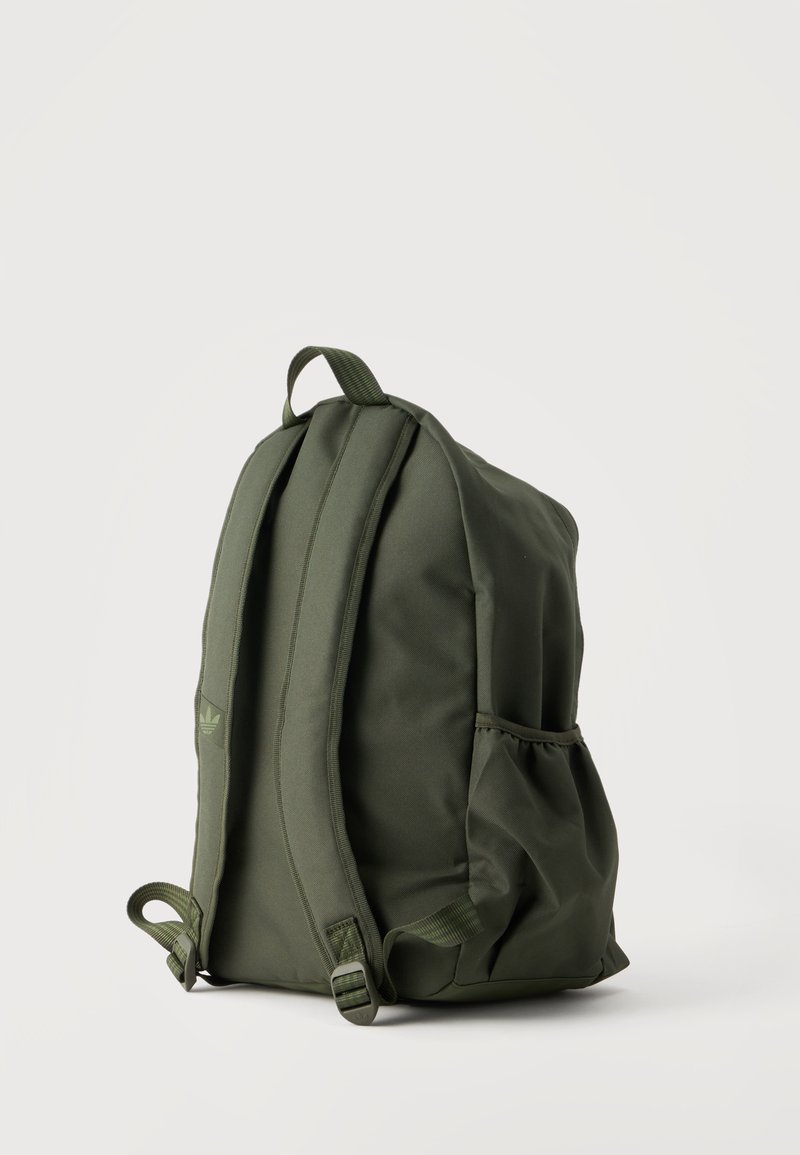 Sac à dos vert olive avec deux bretelles, une poignée supérieure et une poche latérale élastique, présenté sur un fond clair et uni.