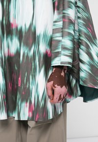 Flowing multicolored fabric top features a vibrant pattern of greens, pinks, and grays, with loose sleeves and a rounded hem.